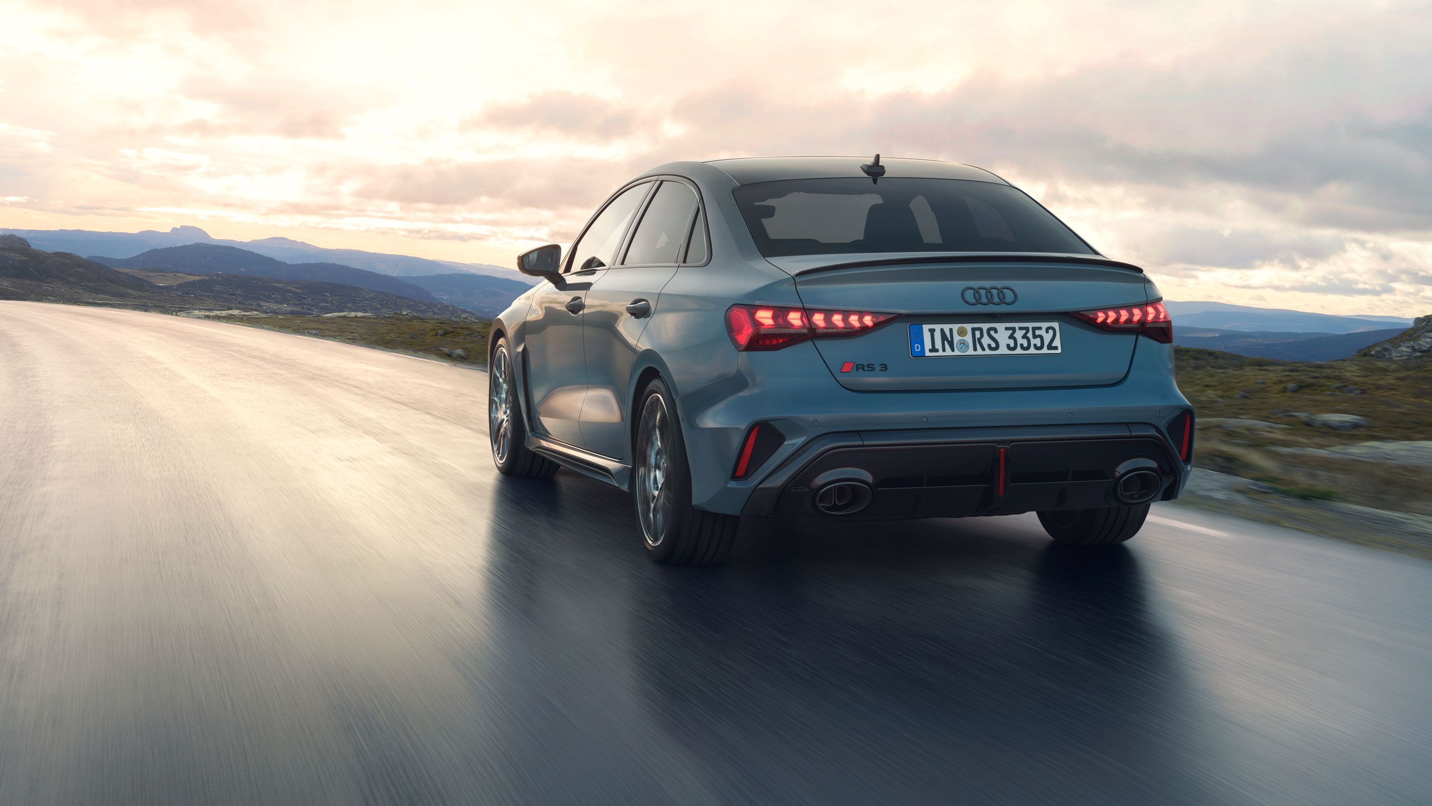 Eine graue Audi RS 3 Limousine fährt eine Landstraße entlang