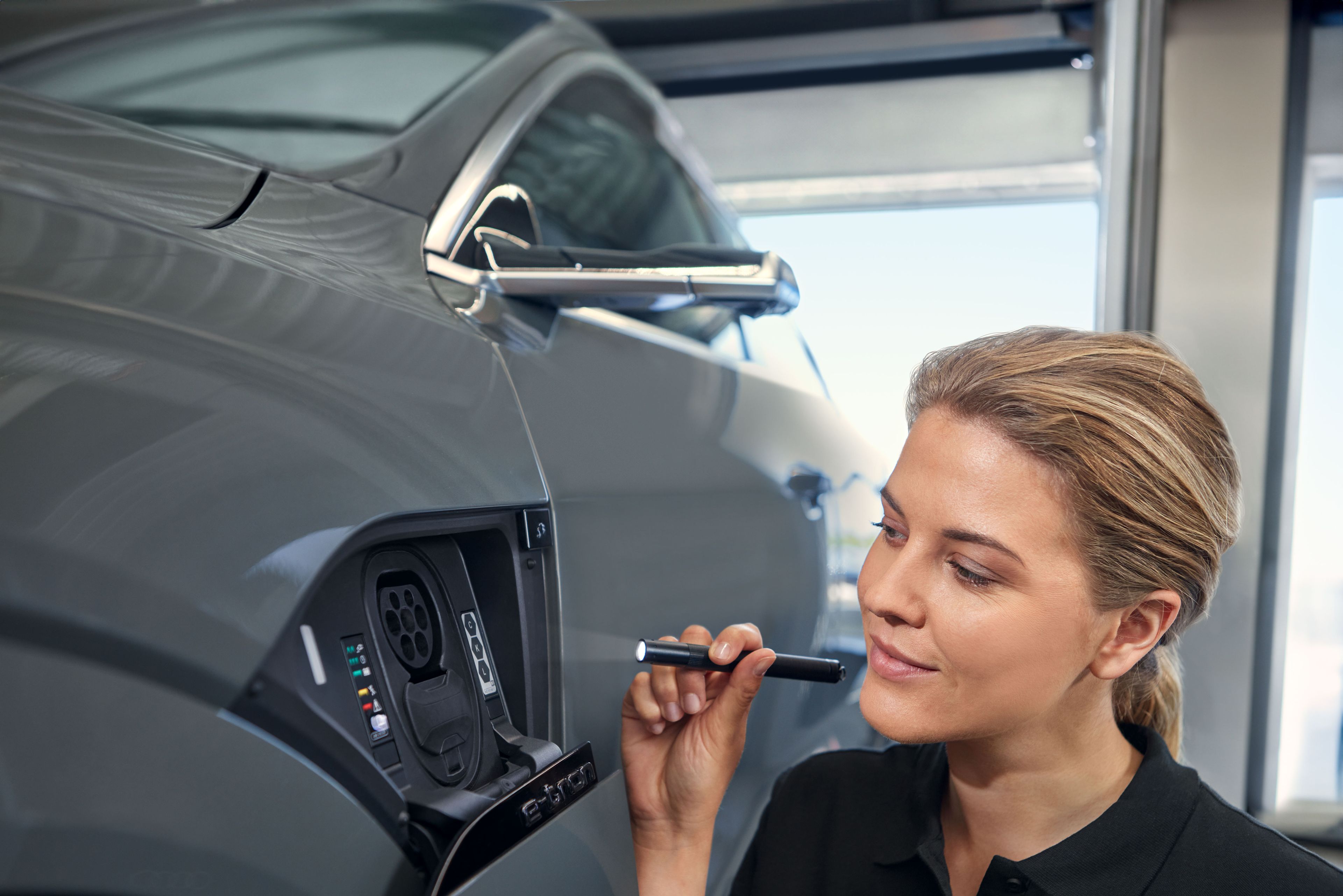 Eine Audi Service Technikerin überprüft den Ladeanschluss eine Audi Elektroautos