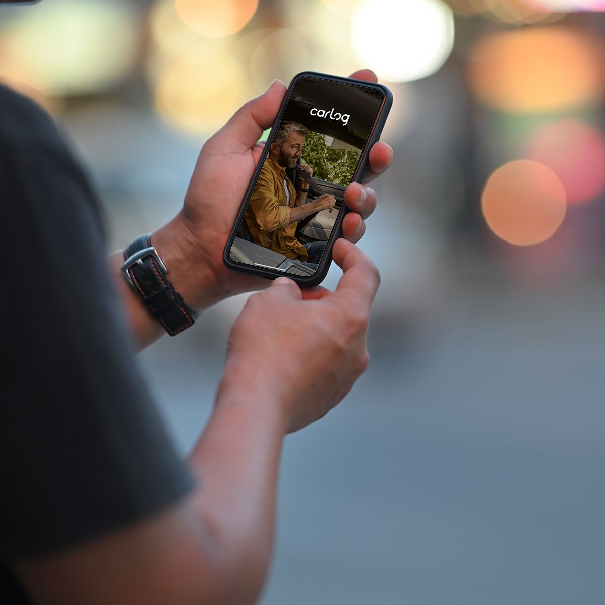 férfi kéz tart egy mobiltelefont amin a carlog látszik