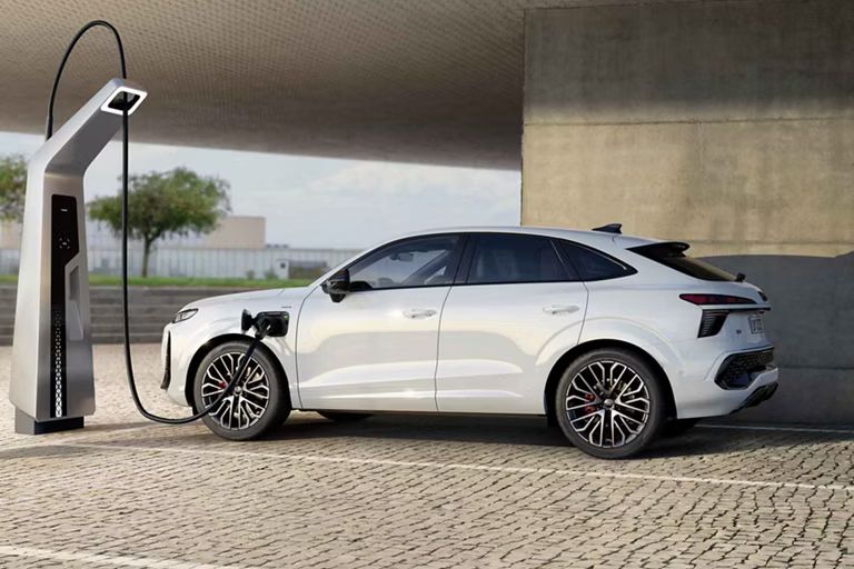 Auf dem Bild ist der Audi Q3 Sportback e-hybrid zu sehen. Dieser steht vor einem Gebäude mit einer Ladesäule und lädt.