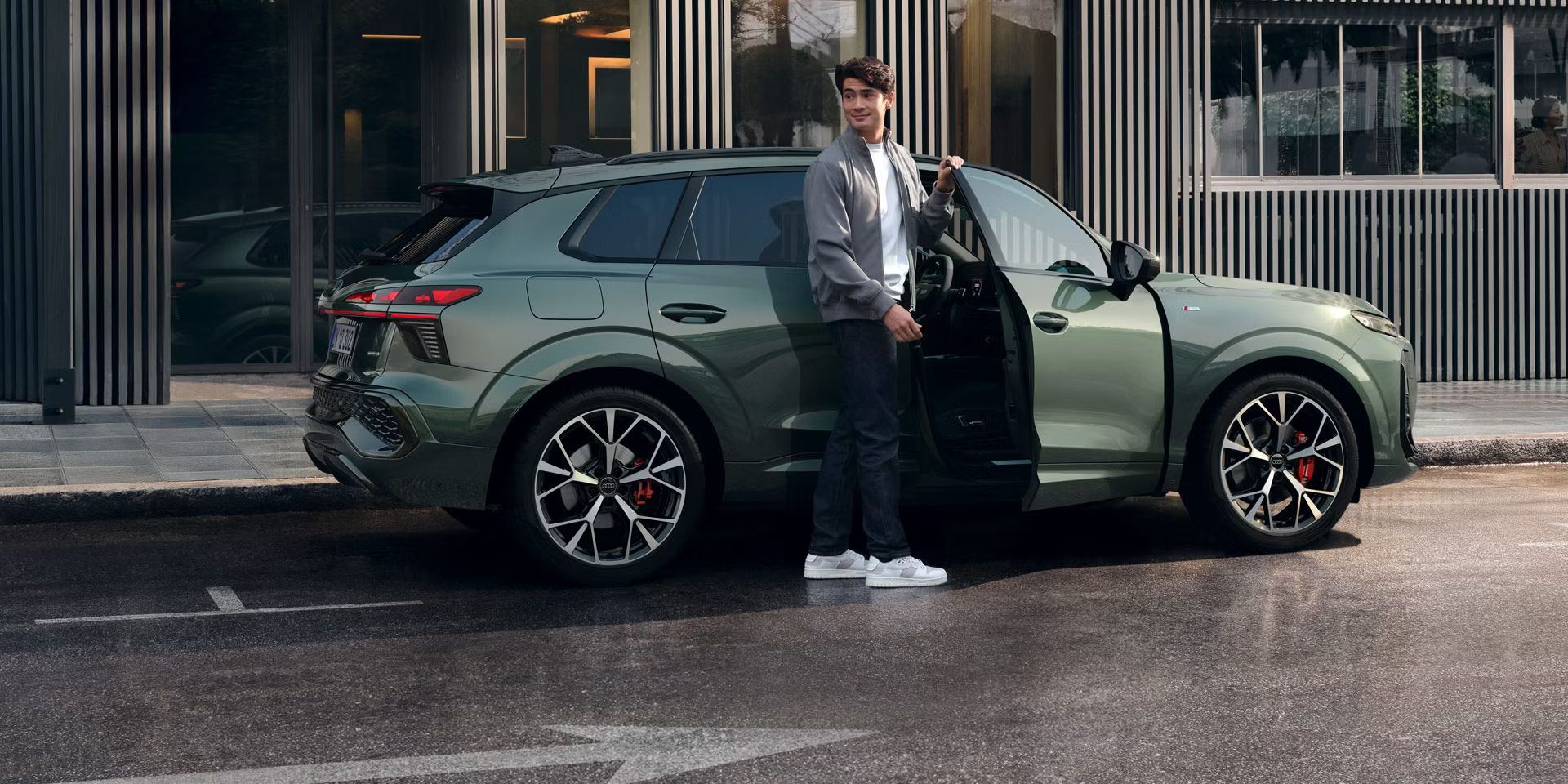  Egy férfi áll egy épület előtt parkoló Audi Q3 terepjáró nyitott utasoldali ajtajánál.