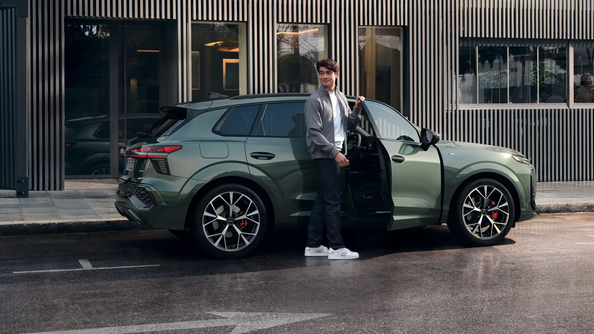  Egy férfi áll egy épület előtt parkoló Audi Q3 terepjáró nyitott utasoldali ajtajánál.