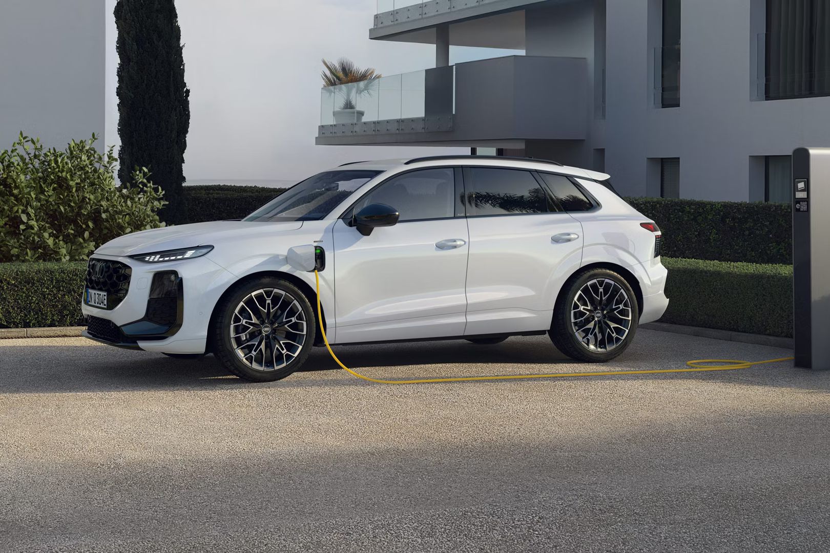 Weißer Audi Q3 SUV e-hybrid steht an der Ladesäule vor einem Gebäude